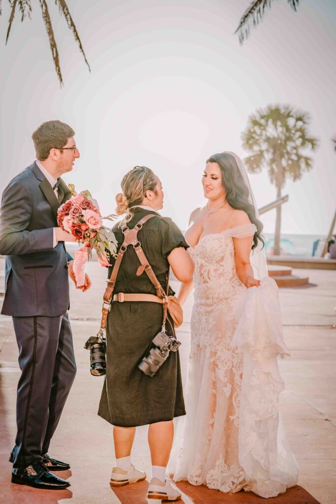 wedding photographer helping bride and groom at sunset