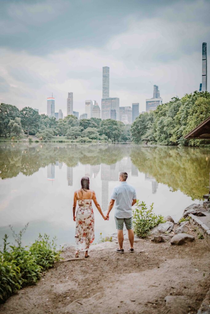man and woman holding hands in central park looking over the lake