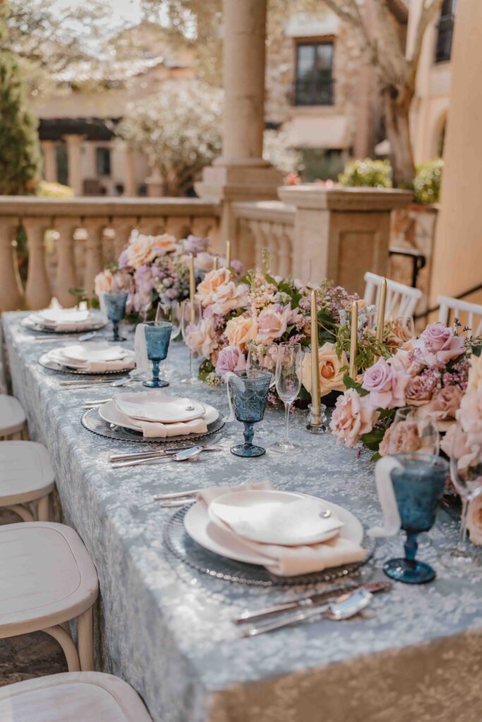 tablescape with white plates, blue tablecloth and glasses and pink flowers
