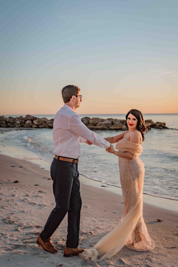 man and woman holding hands and looking at each other during sunset on the beach