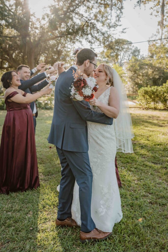 bride and groom kissing while a wedding party behind them cheer