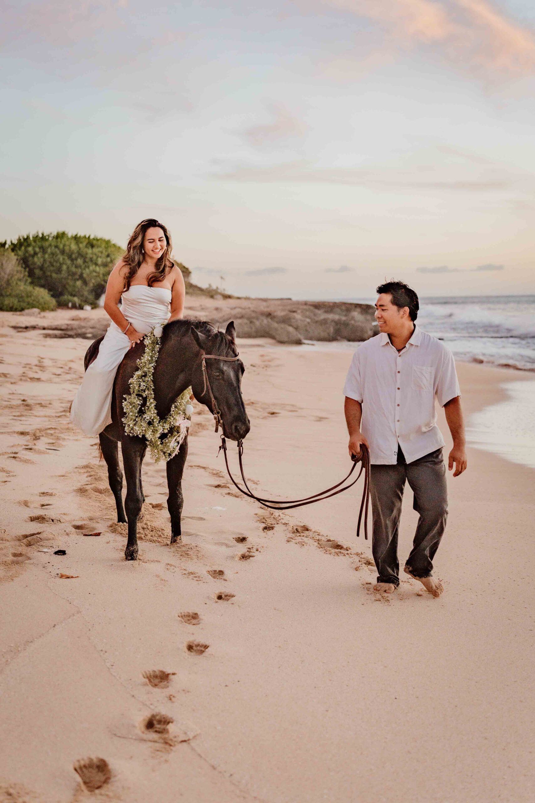 woman on horse lead by man on the beach at sunset