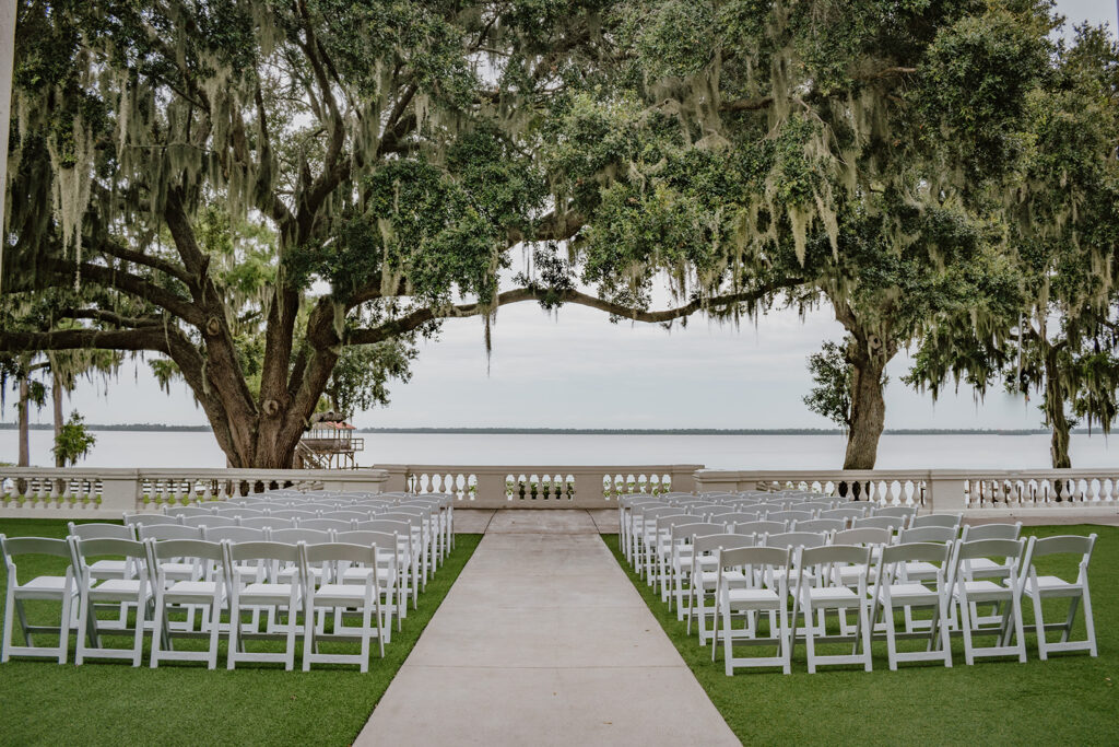 chairs setup up under a tree for a wedding ceremony that are facing the lake
