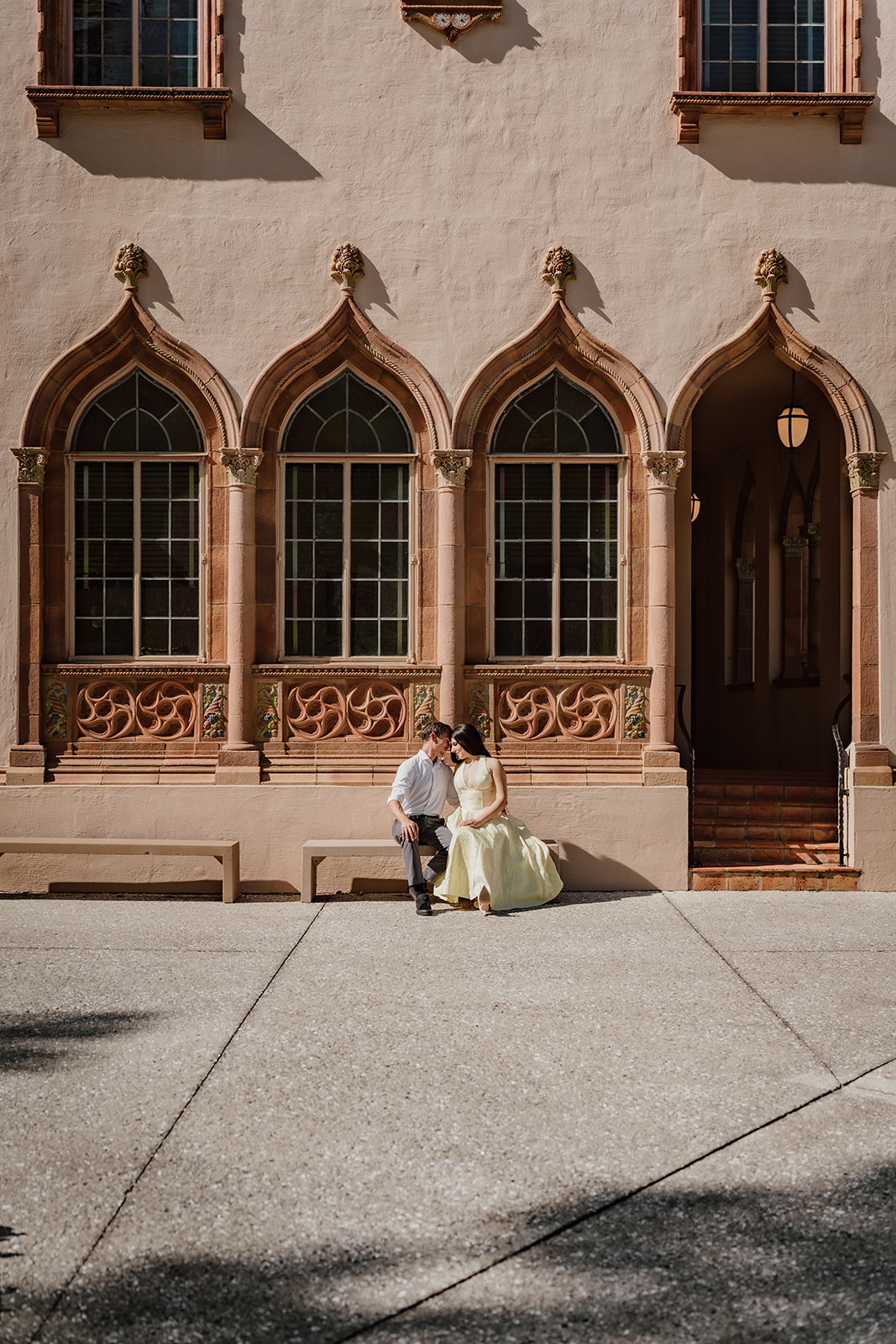 wide shot of man and woman sitting on a bench in front of windows of a museum