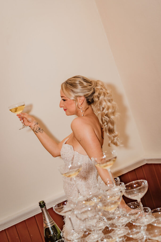 bride holding a champagne glass in front of a champagne tower