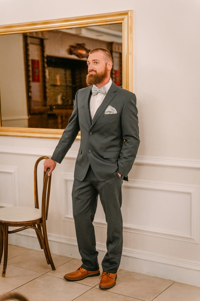 groom in green suit standing by a mirror and chair