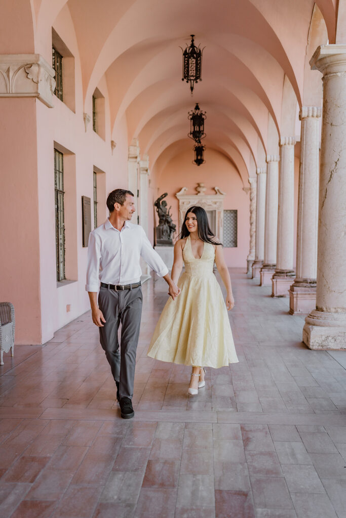 man and woman holding hands walking towards the camera under a cloister at the ringling