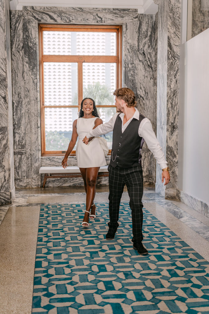 man and woman holding hands running down the hallway
