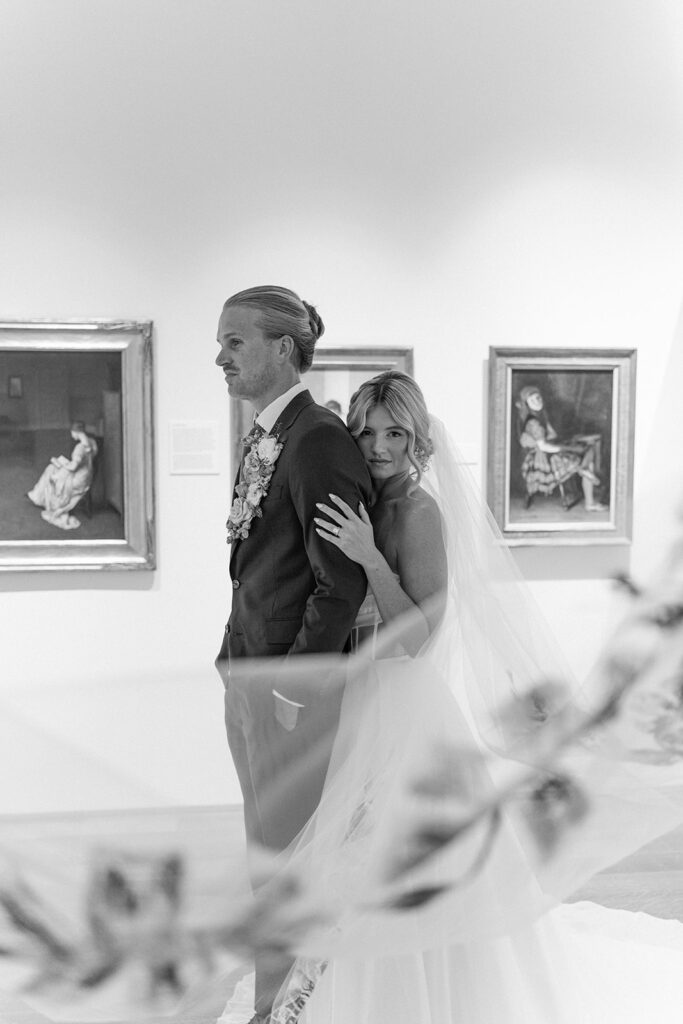 black and white portrait fo a bride and groom in front of art gallery paintings